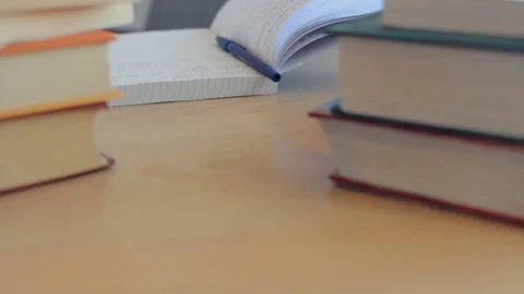 Close up table with pile of books. Student comes, starts studying, taking notes Stock Footage 74987212