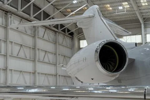 Close up of the tail and engine of a white private jet in a hangar. Stock Photos