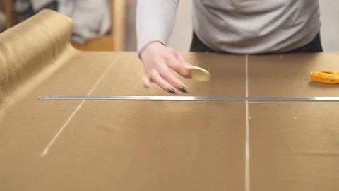 A close-up of a tailor making a pattern with chalk on the dark brown fabric Stock Footage 105475261