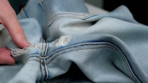 Close-up of tailor's hands checking holes rubbed between legs on women's jeans. Stock Footage 199087499