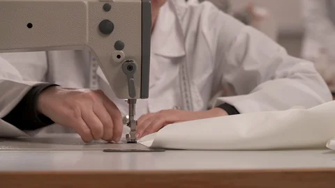 A close-up of a tailor's hands hemming white cloth on the sewing machine  Stock Footage 100331773