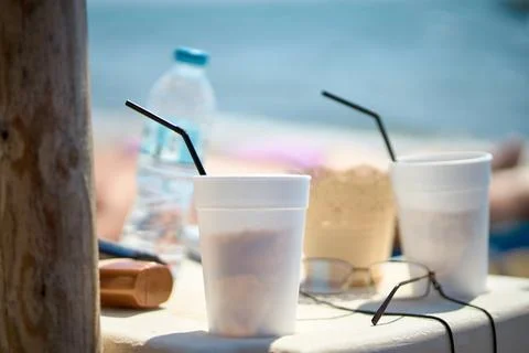 Close-up of take-away cold coffee cups with straws and water bottle on beac.. Stock Photos