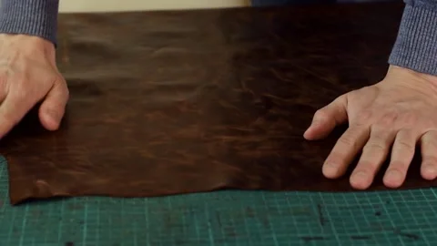 Close-up of a tanner's hands smoothing a sheet of brown genuine leather. Stock Footage 150477603