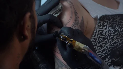 Close up tattoo artist demonstrates the process of getting black tattoo with Stock Footage
