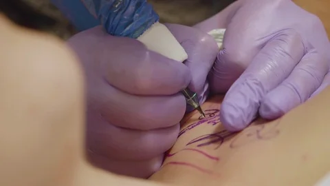 Close up of tattoo artist's hands with tattoo machine tattooing wrhting on Stock Footage