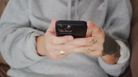 Close-up of tattooed hands using a smartphone while texting or browsing... Stock Footage 318177921