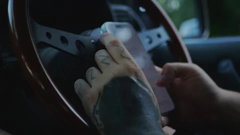 Close-up of tattooed hands using a smartphone inside a car, representing... Stock Footage 341613043
