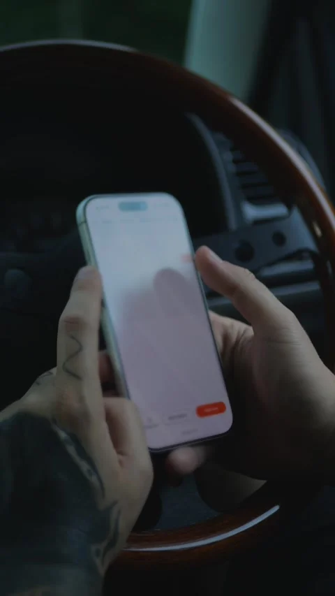 Close-up of tattooed hands using a smartphone inside a car, with... Stockbeeldmateriaal 341613203