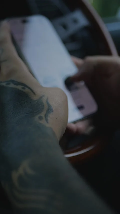Close-up of tattooed hands using a smartphone inside a car, with steering... Stock Footage 341613217