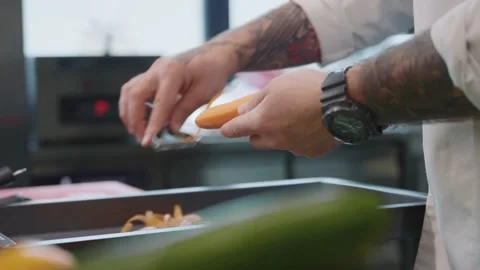 Close-up of tattooed hands of young man peeling carrot for salad. Gourmet Stock Footage 210823024