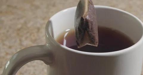 Close up of a tea bag spinning over a brewed cup in slow motion Stock Footage 319045694