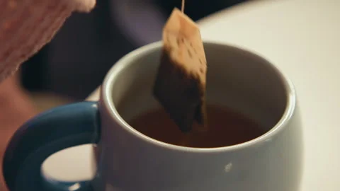 Close-up of tea bag steeping in ceramic mug while amber liquid drips back into Stock Footage 345673605