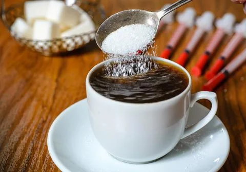 Close-up: a teaspoon with sugar falling into a Cup of coffee. Amid the chunks Stock Photos