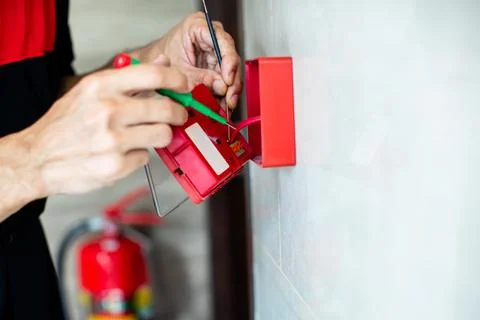 Close-up of technician hands installing and wiring a red fire alarm manual .. Stock Photos