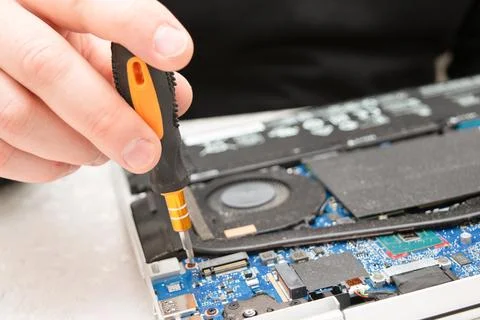 Close-up of a technician's hand using a screwdriver to repair a laptop moth.. Stock Photos