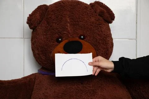A close-up of a teddy bear, with a child's hand holding a piece of paper with Stock Photos
