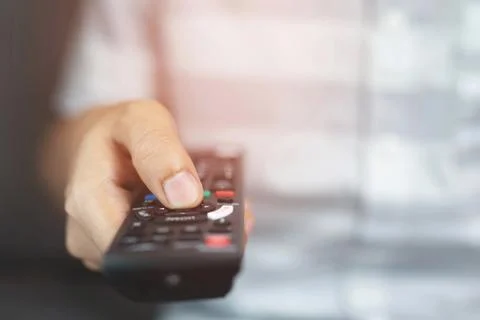 Close up Television remote control in casual man hands pointing to tv set a.. Фото