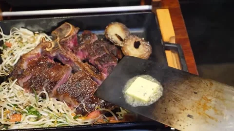Close-Up of Teppanyaki Chef Cooking T-Bone Steak with Butter and Noodles on Hot 스톡 동영상 332817426