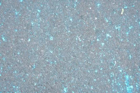 Close-up texture of asphalt with small bright blue flecks and a single leaf 스톡 사진