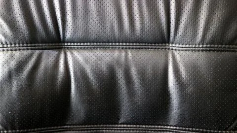 Close up texture of black perforated leather upholstery with stitched seams.. Stock Photos