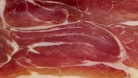 Close-up texture of a slice of cured jamon, marbled pattern of meat and fat Stock Photos
