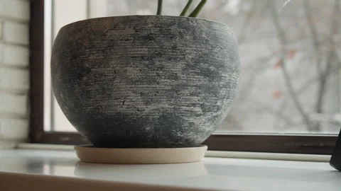Close up of textured gray pottery plant pot on white windowsill with frosted Stock Footage 344874746