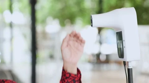 A close-up of a thermometer with a user reaching out to the sensor to measure Stock Footage 154326138