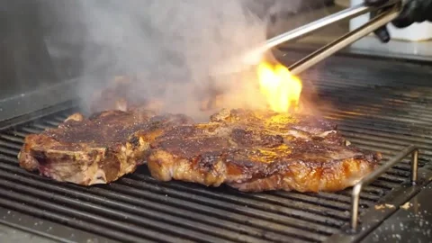 Close-up of Thick Beef T-Bone Steaks Sizzling on a Hot Charcoal Grill with Smoke Vídeos de archivo 332815175