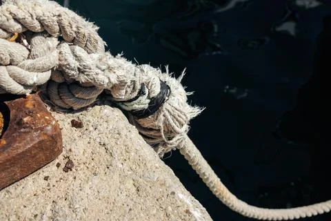 Close-up of a thick marine rope secured on a concrete dock by the sea Stock Photos
