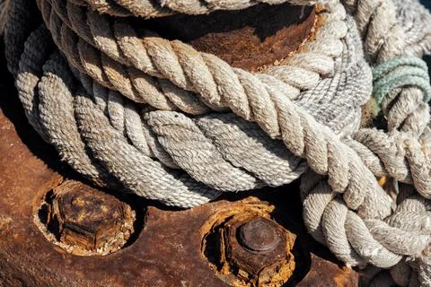 Close-up of thick nautical ropes wrapped securely around a rusty metal moor.. Stock Photos