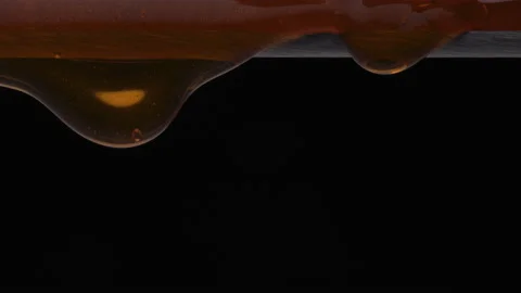 Close up of thick orange color liquid dripping over an edge on a black Stock Footage 201336200