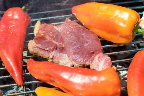 Close-up of a thick pork steak grilling on a hot metal grate with bell pepper 库存照片