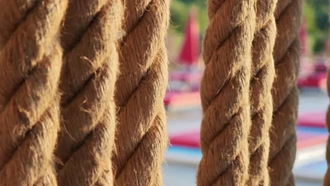 Close up of thick ropes hanging vertically, with blurred beach club in Vidéo 312122539