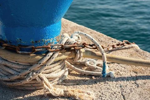 Close-up of thick white mooring rope and rusty metal chain tied around blue.. Stock Photos