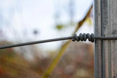 Close up of a thick wire tied securely around a galvanized steel fence post Stock-Fotos