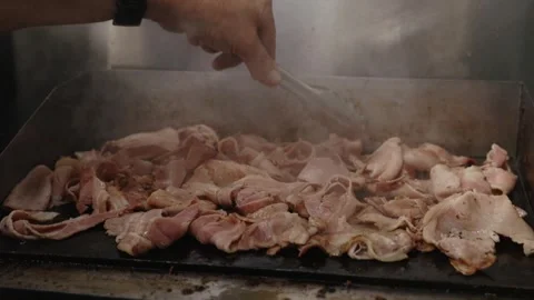 Close-up of thin-cut streaky bacon rashers cooking on a flat top grill, showing 스톡 동영상 332617511