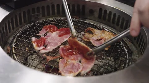 Close-up of thin marinated meat slices grilling on a metal round grate over.. Stock Footage 338394640