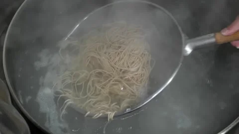 Close-up of thin noodles being boiled in a stainless steel strainer basket in a Stock Footage 333523921
