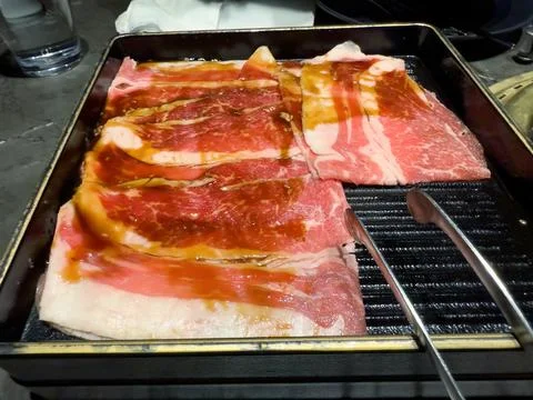 Close up of thinly sliced raw fatty beef meat in tray next to a Japan BBQ s.. Stock Photos