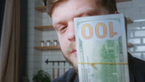 Close-up of a thoughtful man looking at a stack of hundred-dollar bills, re.. Stock Footage 310876619