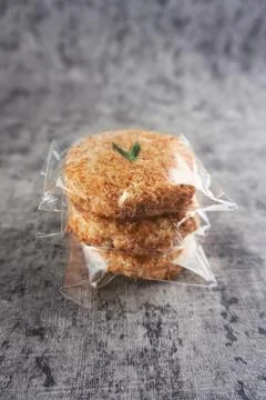 Close-Up of Three Coconut Cookies in Plastic Wrapping on Grey Background. S.. Foto stock