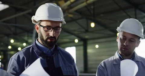 Close up of three engineers in helmets with big paper drawings having a talk and Stock Footage 84420412