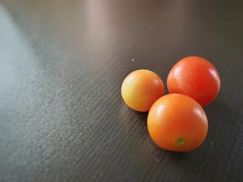 Close-up of three fresh cherry tomatoes on a dark textured table Stock Photos