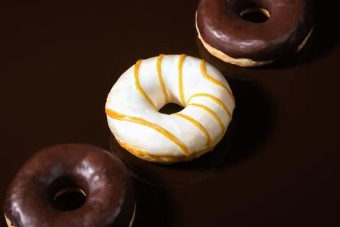 Close-up three glazed donuts are lying on diagonal on dark chocolate backgr.. 写真素材