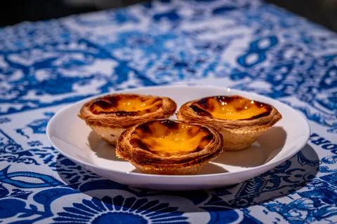 Close-up of three pastel de nata custard tart on blue tablecloth on sunny day Stockfoto's