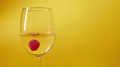 Close up. Three raspberries falling into glass of white wine alcohol over yellow Stock Footage 149694751