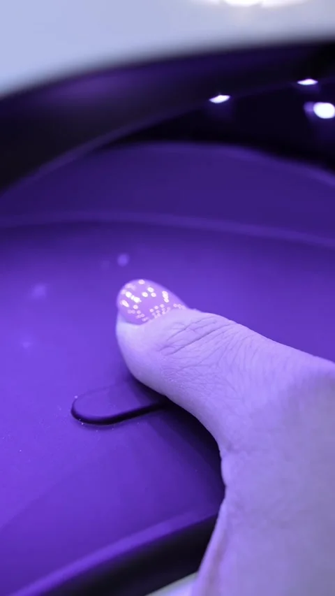 Close-up of a thumb curing under a UV nail lamp, with purple LED glow Vidéo 333654476