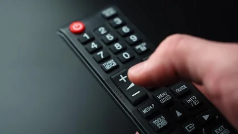 Close-up of a thumb pressing volume down on a TV remote control on a dark Stock-Footage 329596952