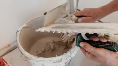 Close-up of a tiler loading adhesive onto a notched trowel during an indoor Stock Footage 345832985