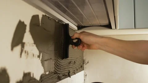 Close-up of a tiler using a notched trowel to apply tile adhesive to a wall Stock Footage 344563768